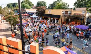 Crowded streets of downtown Clemson on game day, showcasing a vibrant scene with fans in Clemson University colors, festive decorations, and local shops bustling with activity.